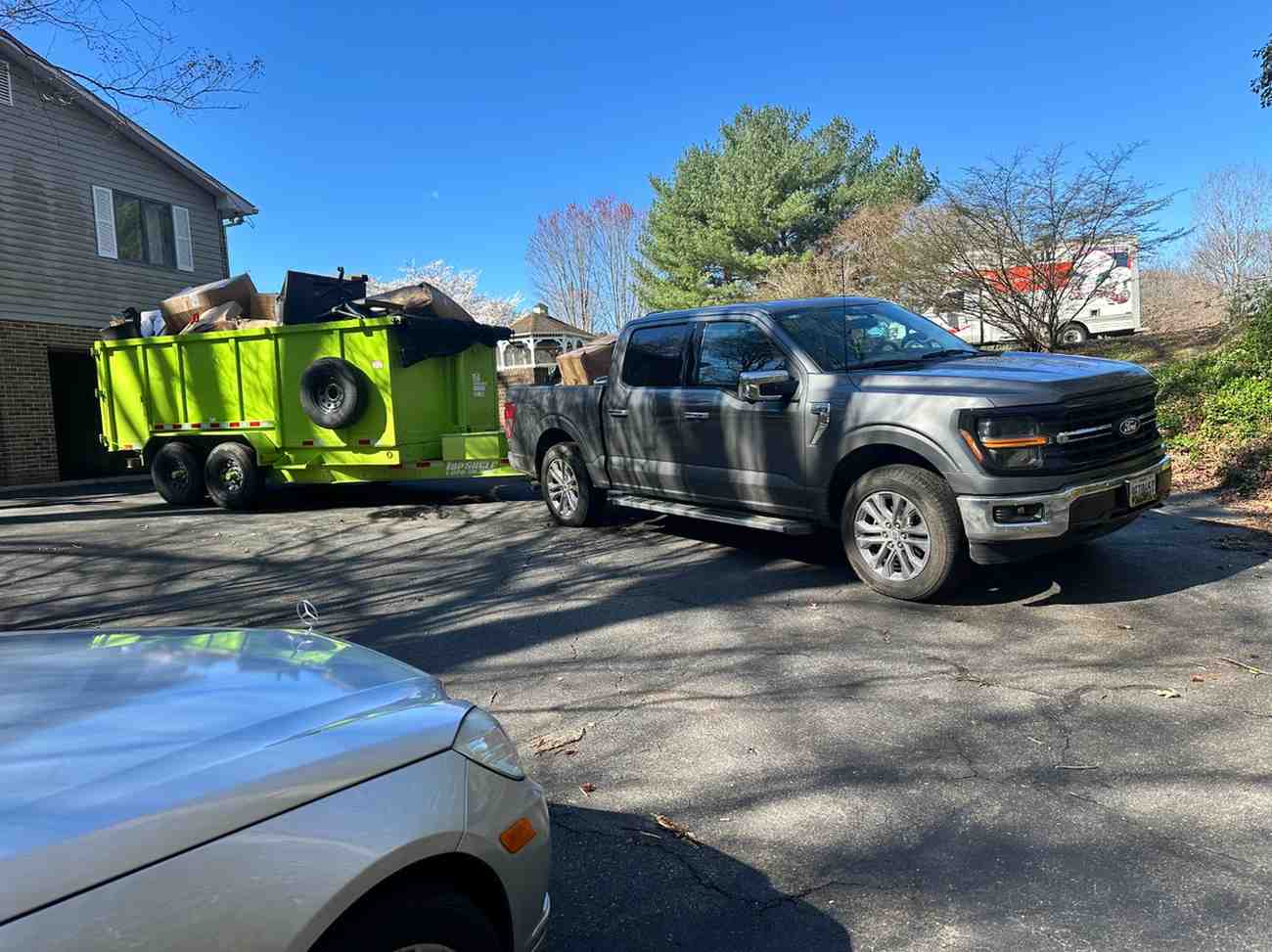 Loaded green dump trailer and pickup truck in a driveway after a house cleanout